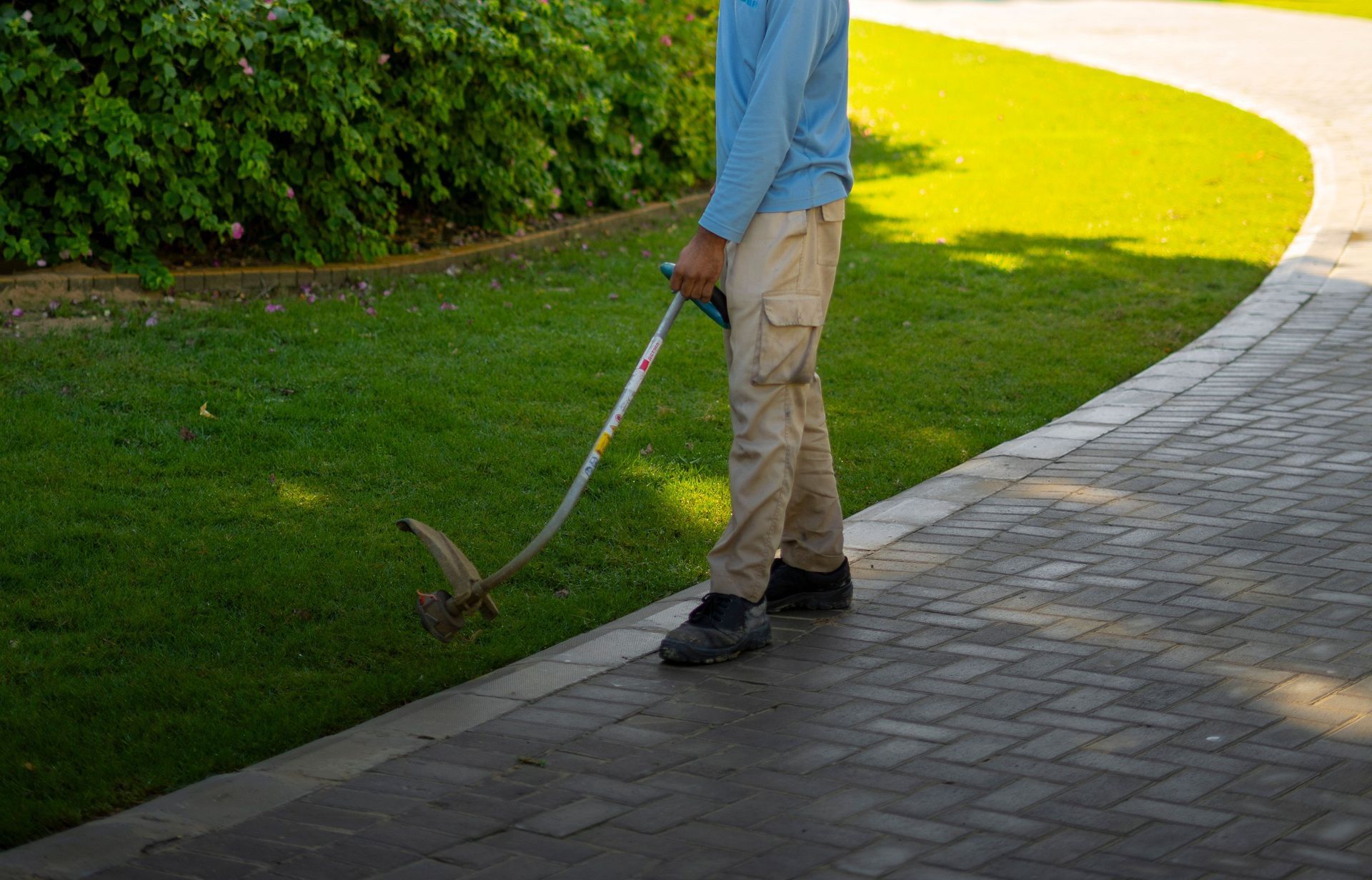 Man trimming lawn in a sunny Dubai park, surrounded by lush greenery and flowers.